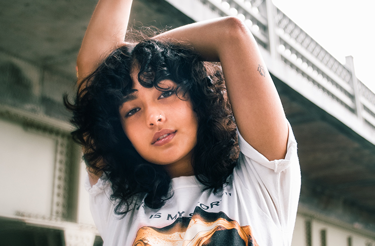Woman with curly hair standing with her hands in the air.